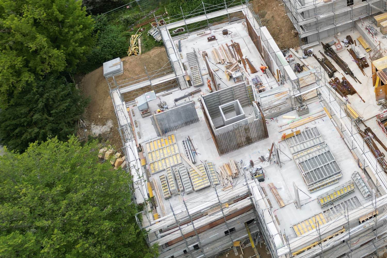 Luftaufnahme eines Hauses im Rohbau mit Gerüst, links Bestandesbäume
